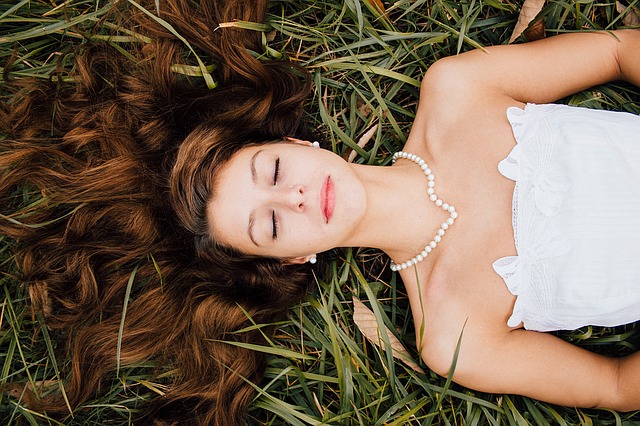 Briderelaxing on grass in white dress with pearls, staying calm on your wedding day